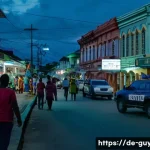 가이아나 치안 상황 - A bustling urban street scene in Georgetown, Guyana, at dusk with a diverse group of people walking ...